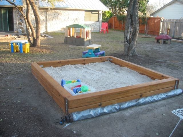 A child raking a sandbox next to his nanny