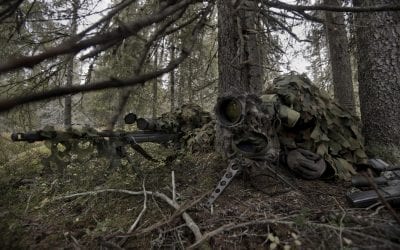 A man lying on a hill looking through a rifle scope